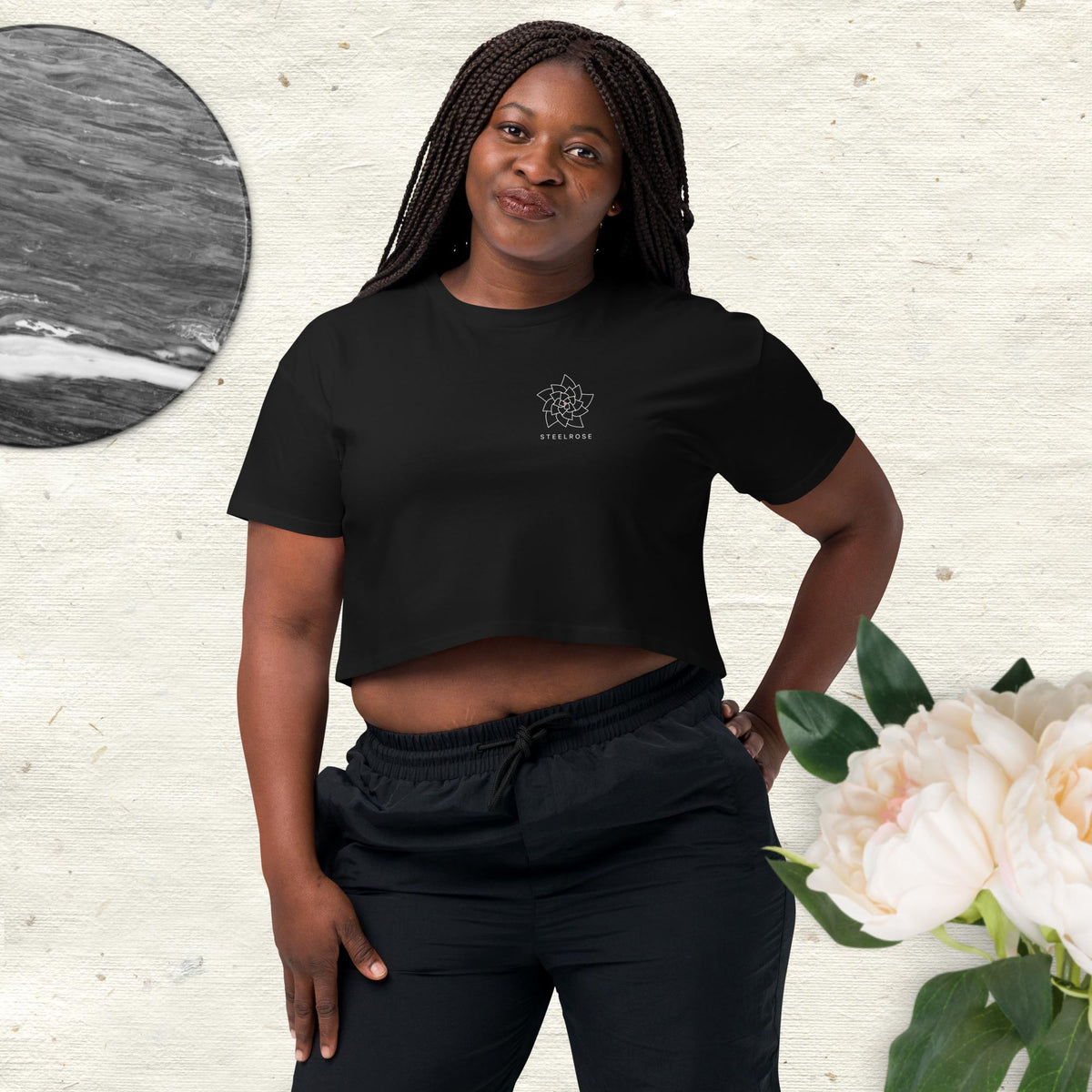 Woman wearing the STEELROSE Signature Crop Tee in black on cream linen with white peonies and marble